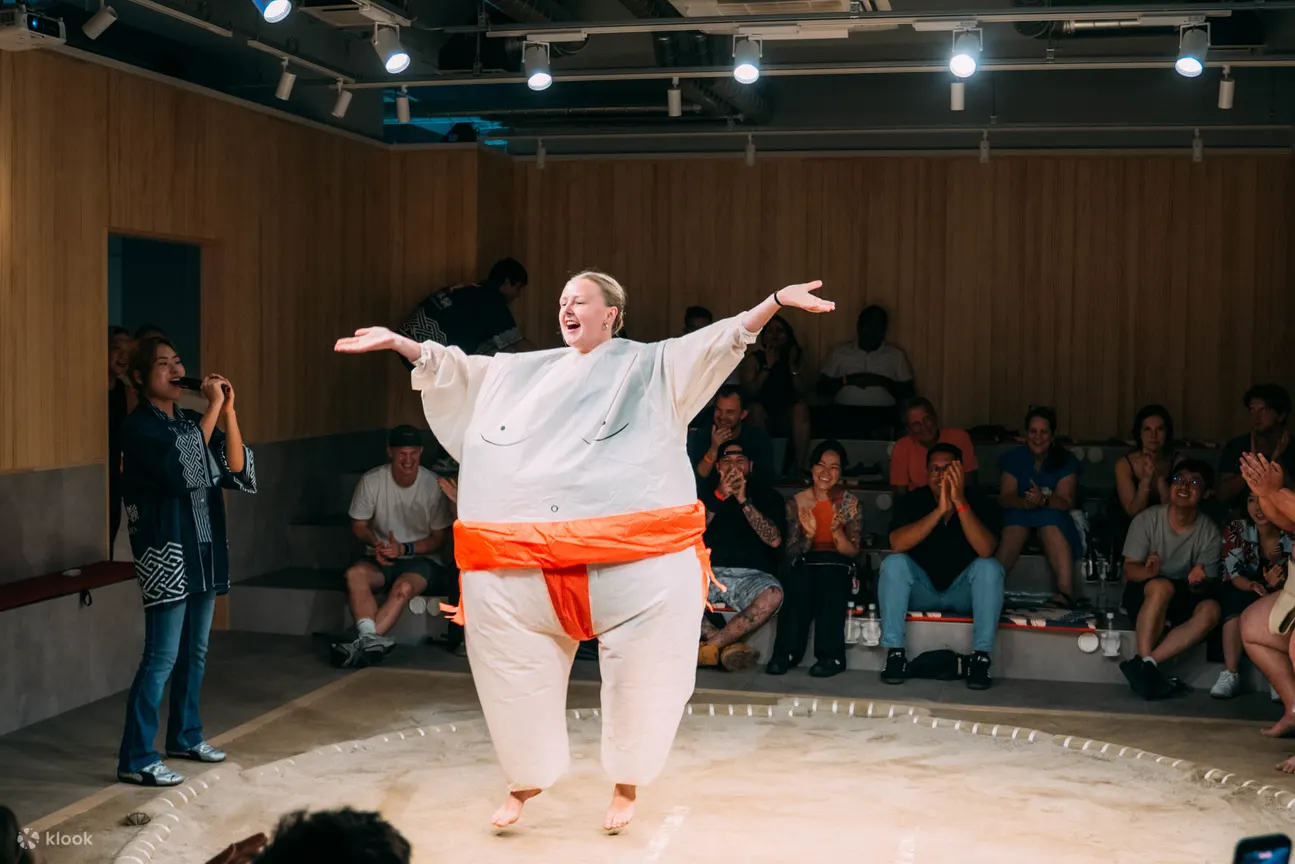 A delighted visitor in an inflatable sumo suit celebrating in the ring as the audience cheers