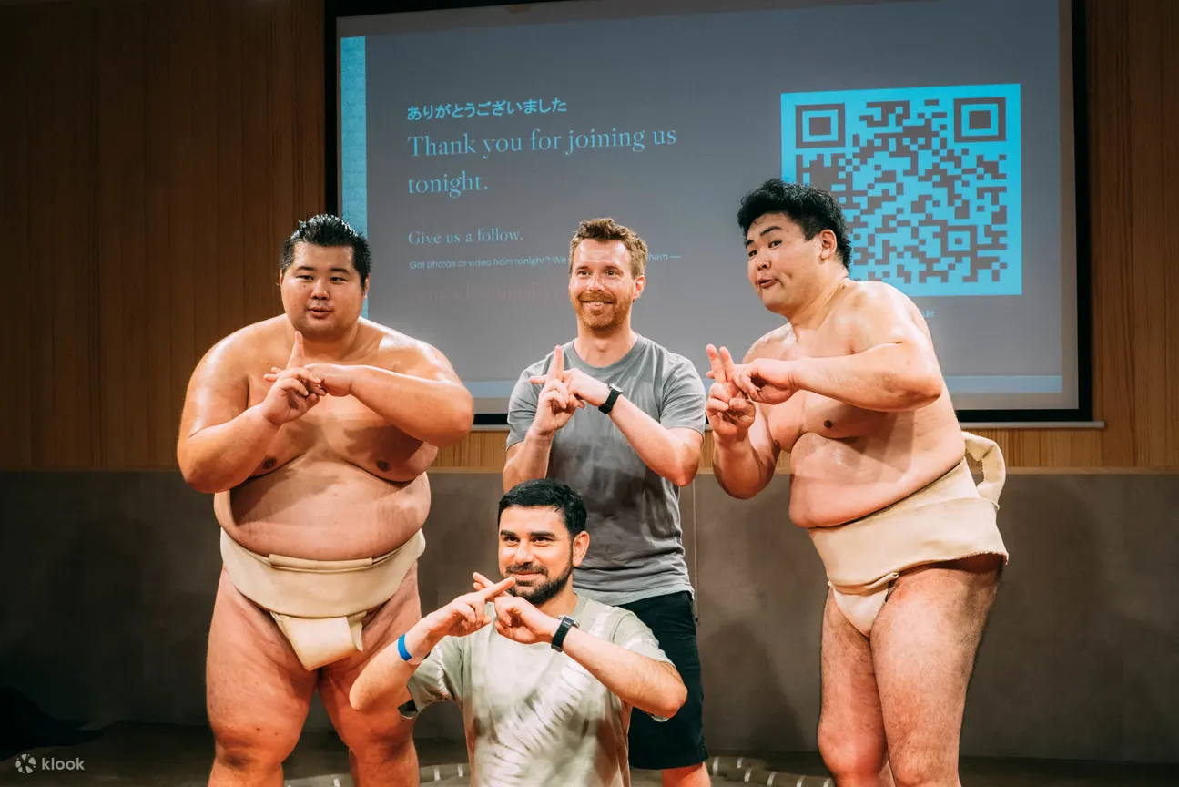 Guests posing for a group photo with two sumo wrestlers, everyone making the sumo finger-frame pose